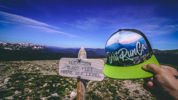 dirt run co trucker hat with a 12,000 foot mountain sign behind it