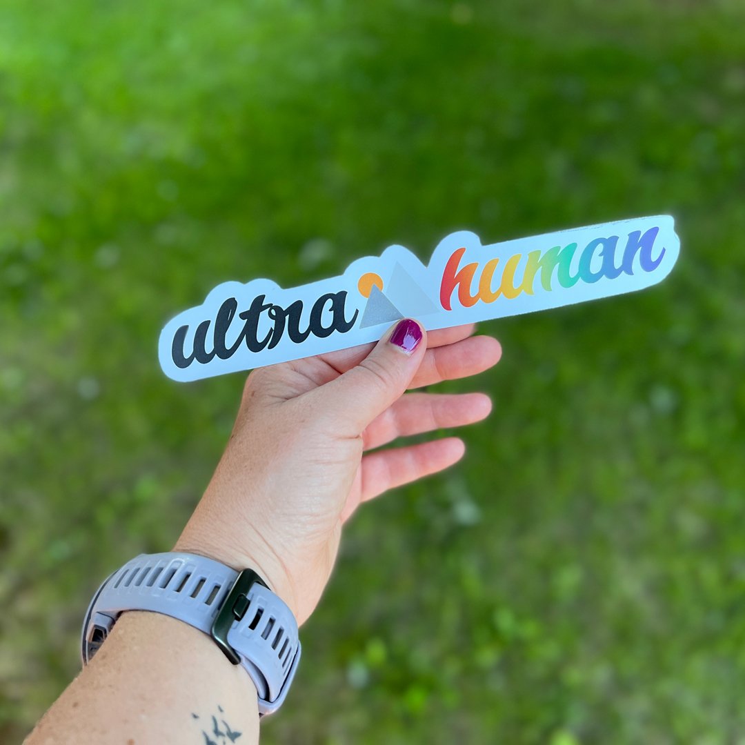 a woman holding an ultra human pride sticker from monolith trail co